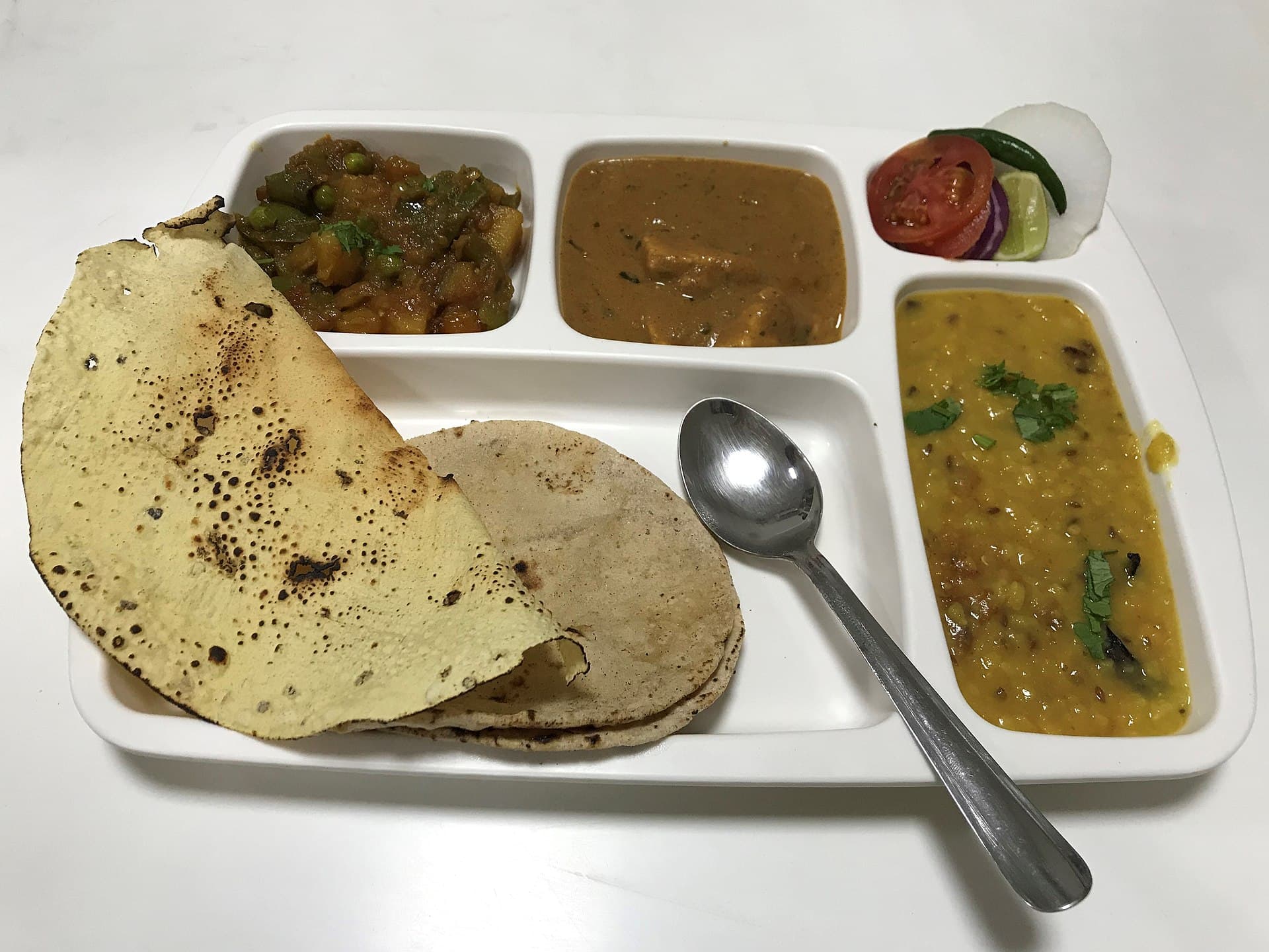 A dal and paneer combo meal with roti, rice, and sides